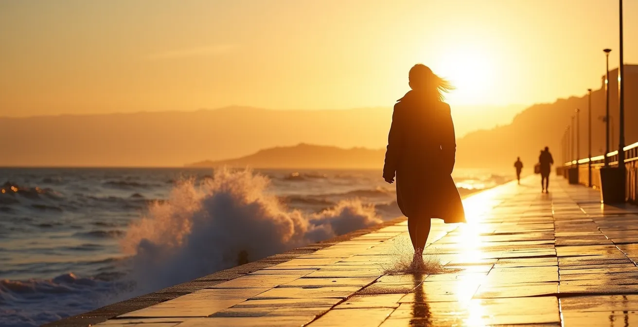 Promeneur solitaire sur une digue au moment de la marée montante avec embruns et lumière dorée